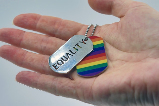 hand holding dog tags, one that is rainbow and one that says equality