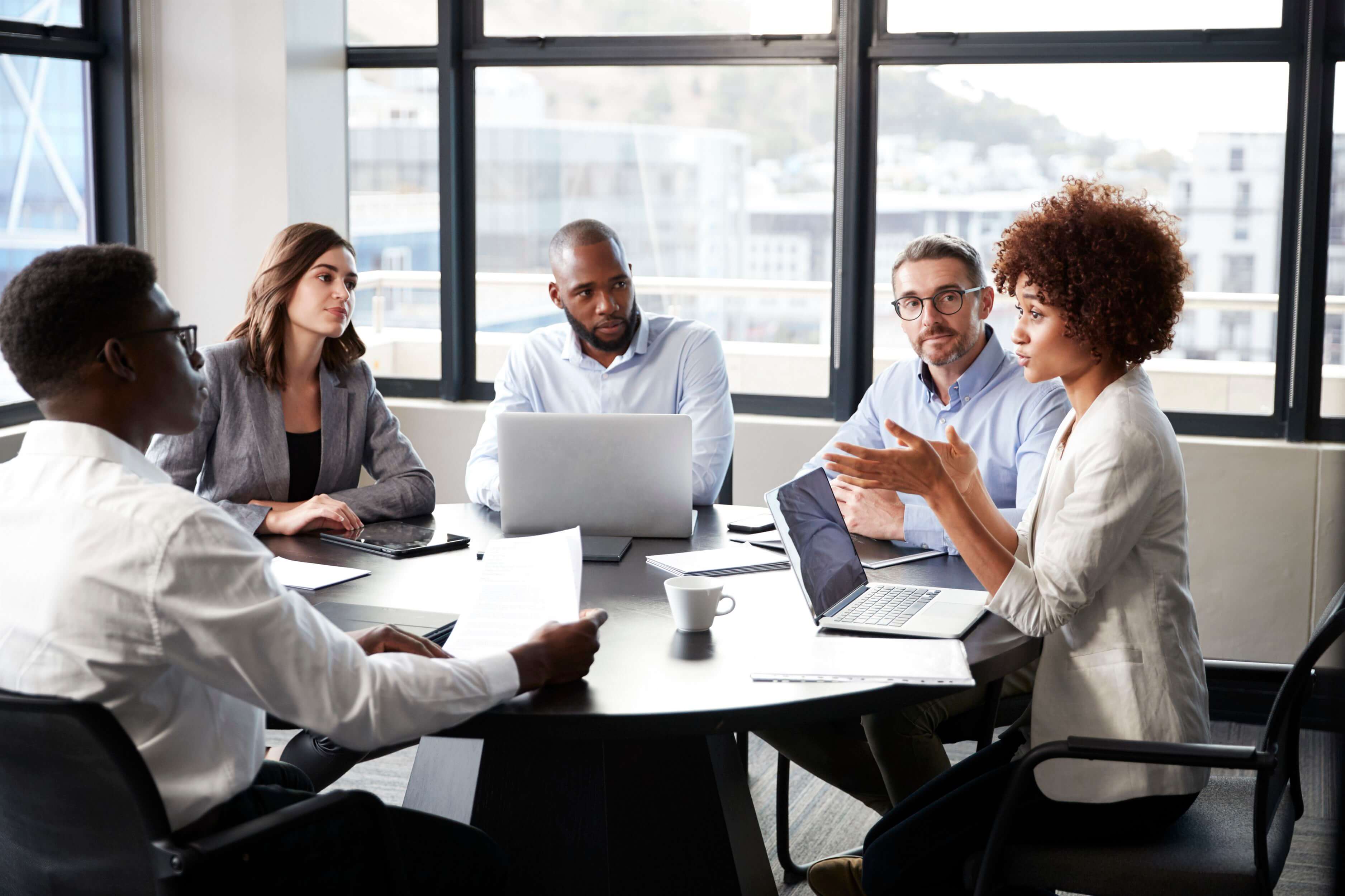 Woman presenting to an attentive boardroom, reflecting dynamic and inclusive leadership skills.