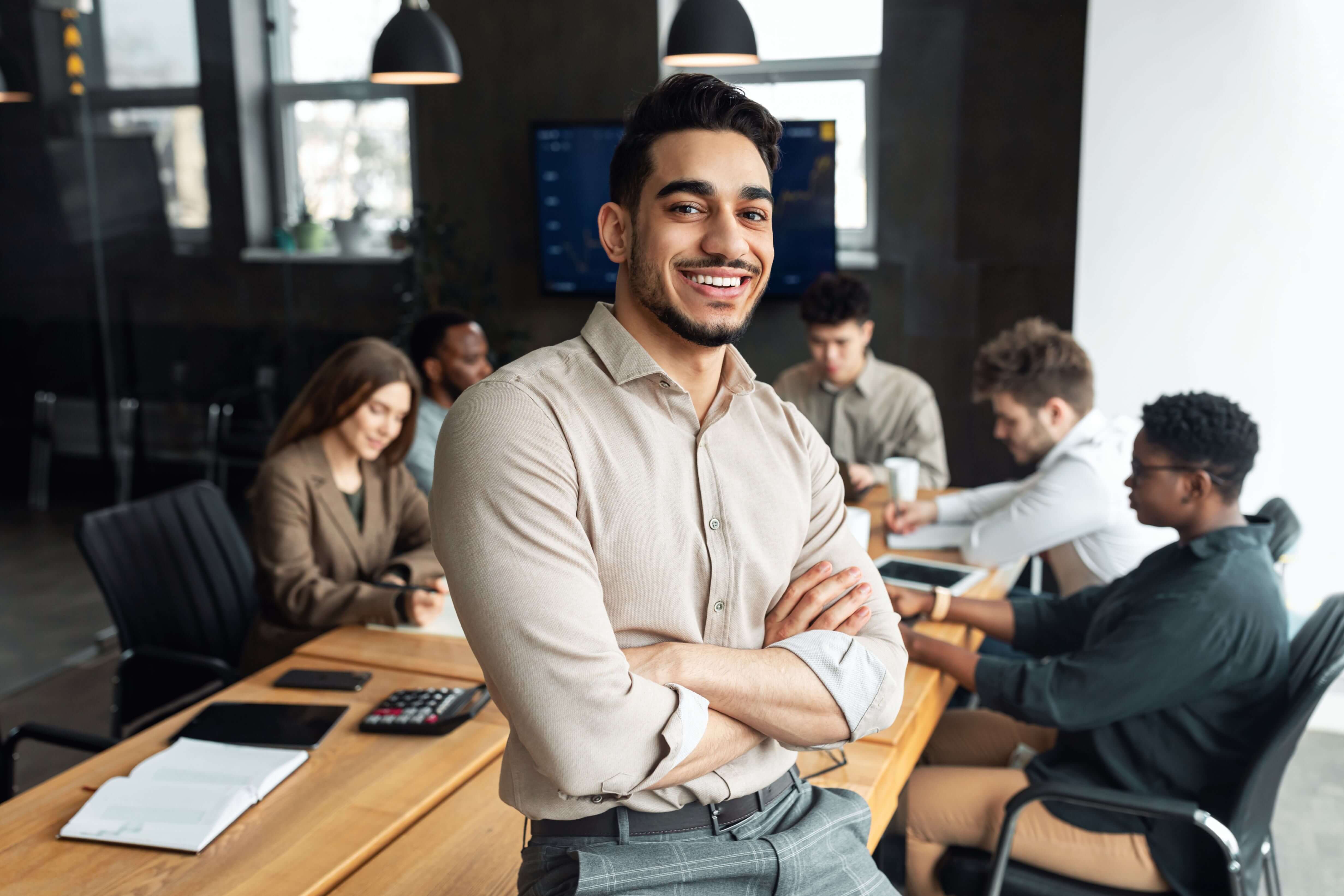 Business casual man in a meeting, leaning on a boardroom table, representing relaxed yet effective leadership communication.