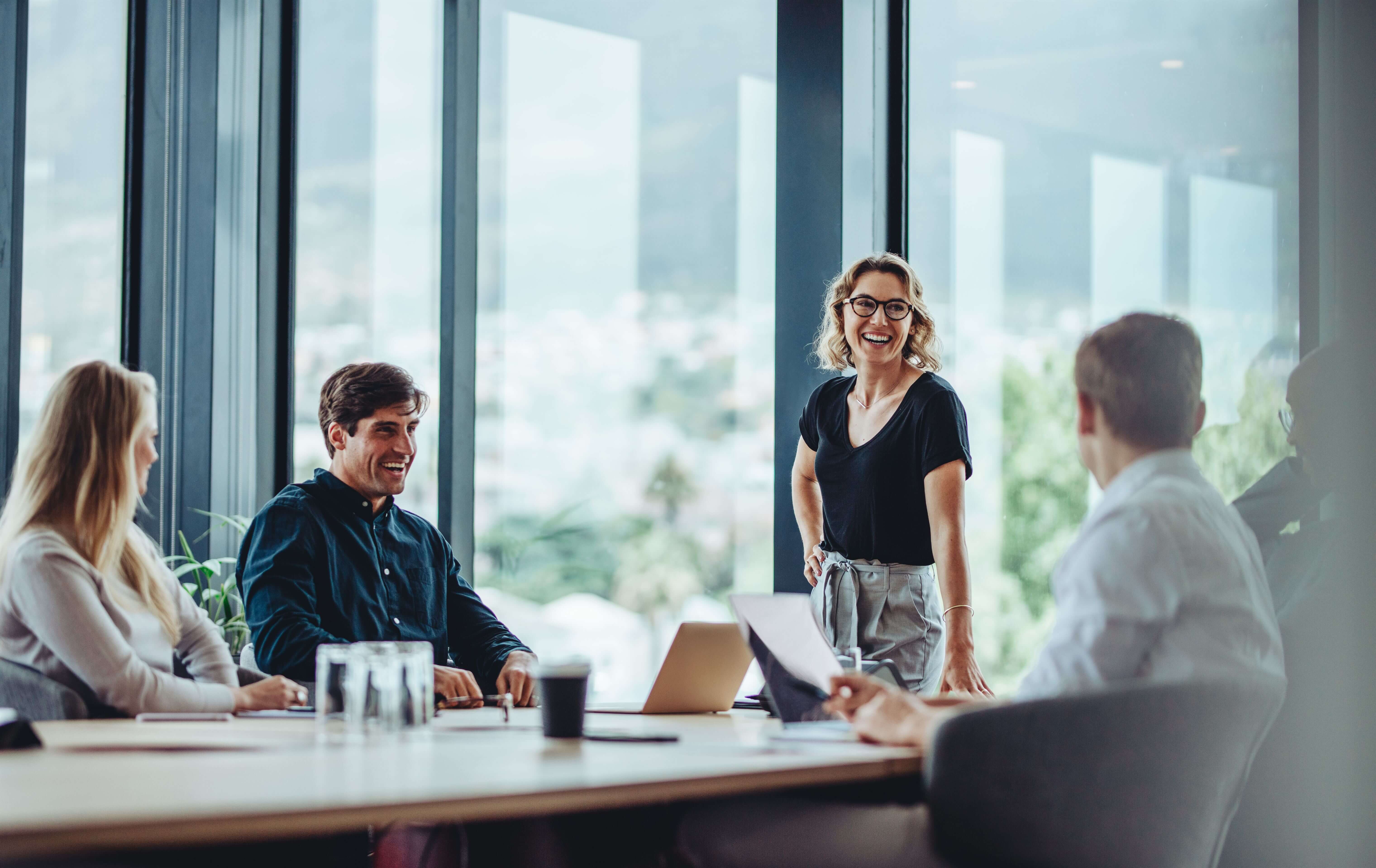 Business casual executive woman presenting to a smiling group, embodying 'Speaking As A Leader' traits for influential leadership.