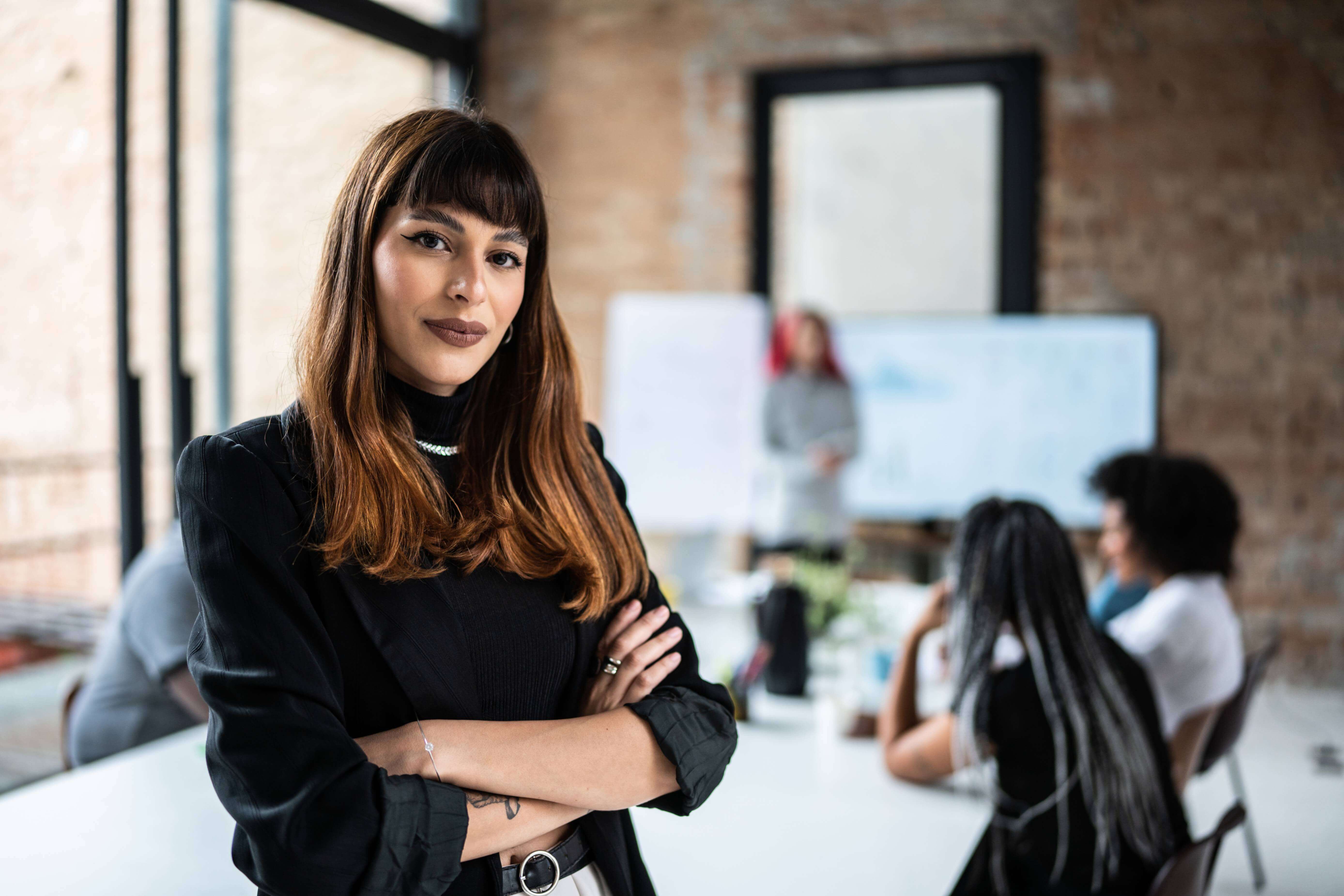 Professional woman with a tattoo in a blazer, in an office setting, showcasing a blend of seriousness and approachability in leadership.