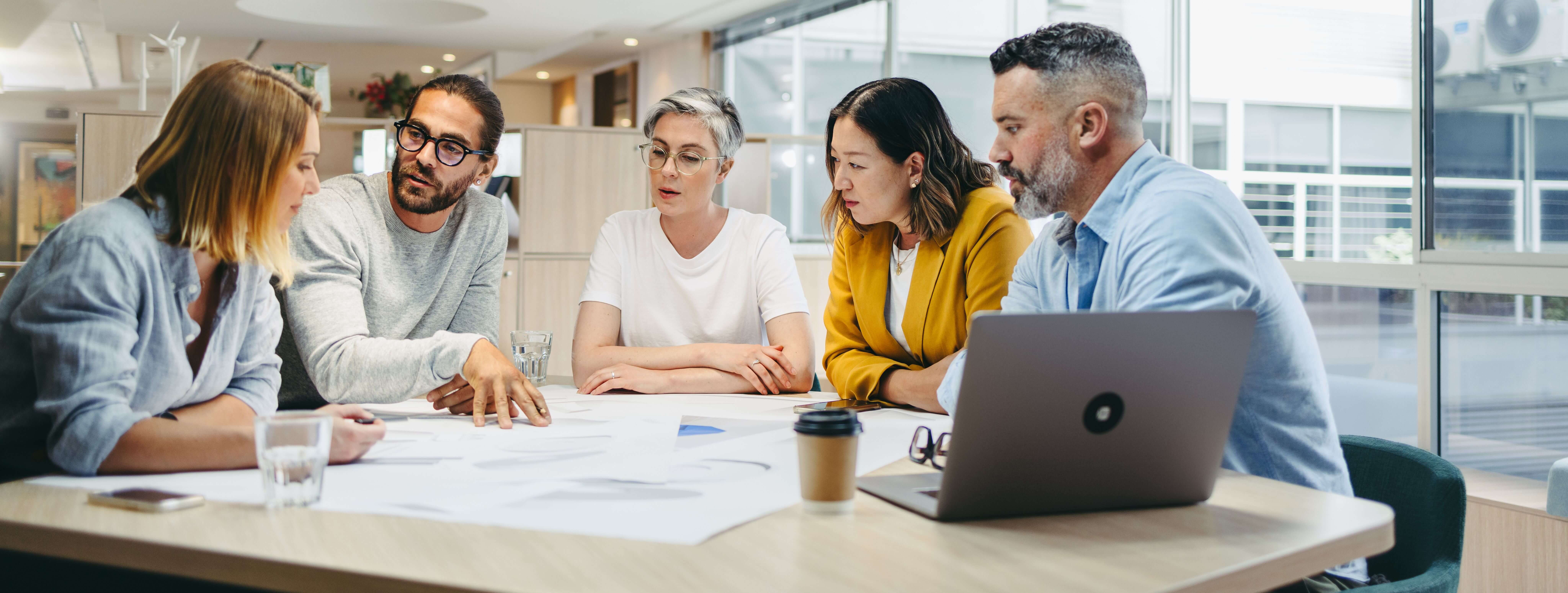 Corporate team with a mix of ages, led by an younger man, in a moment of collaboration, highlighting authentic leadership dynamics.