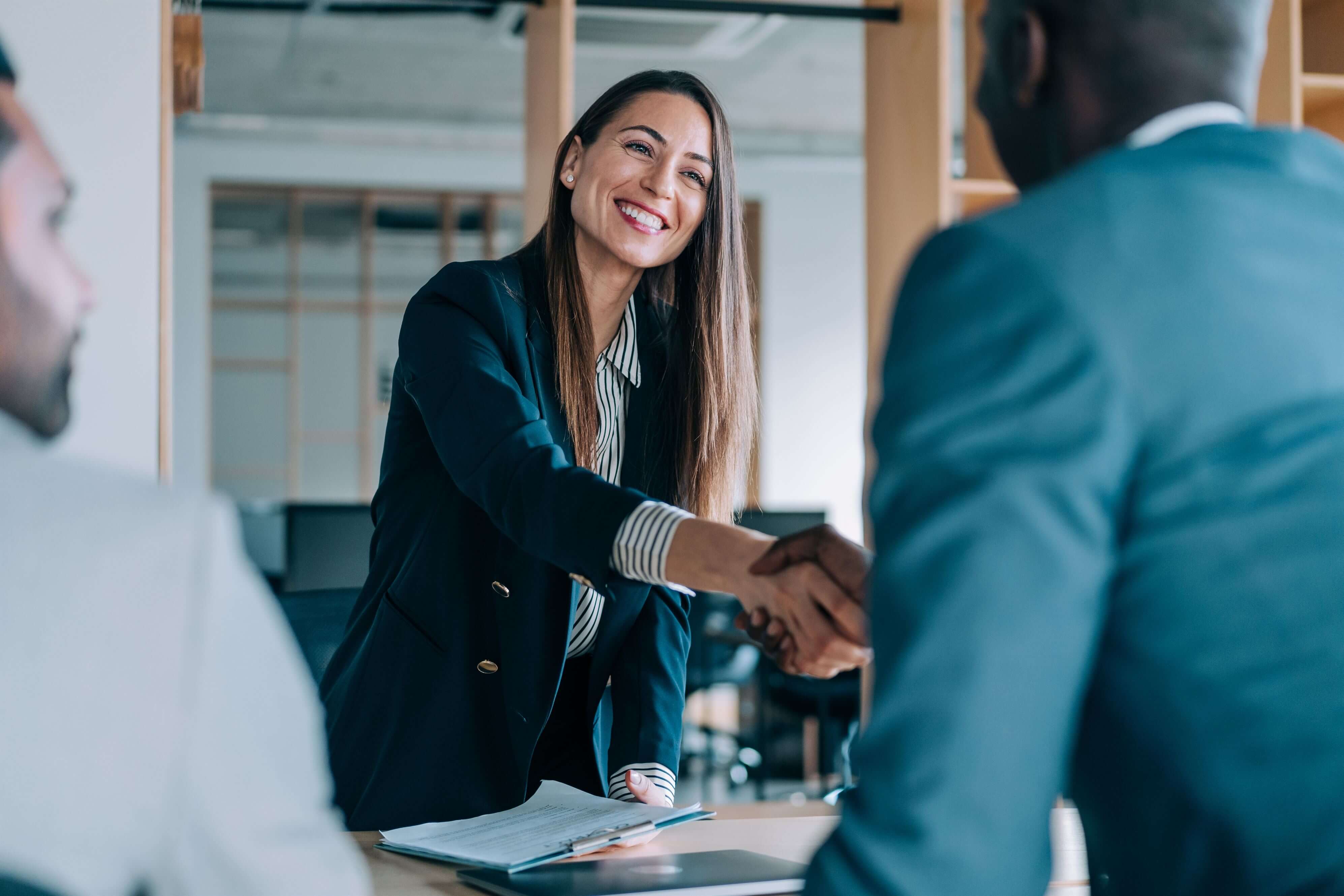 Two professionals in a workplace shaking hands firmly, reflecting a successful agreement or partnership.